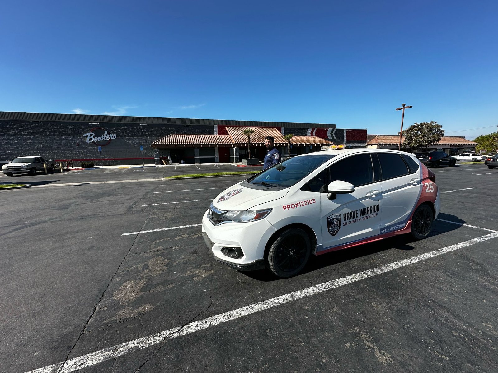 Brave Warrior officer and branded security patrol vehicle in a commercial parking lot